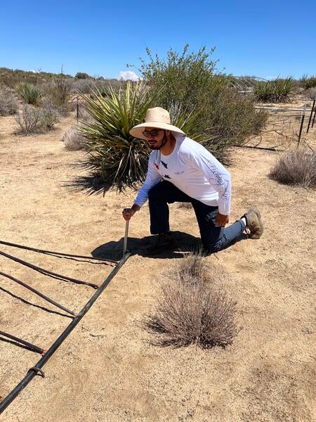 Man with hat kneeling with stake in ground outdoors